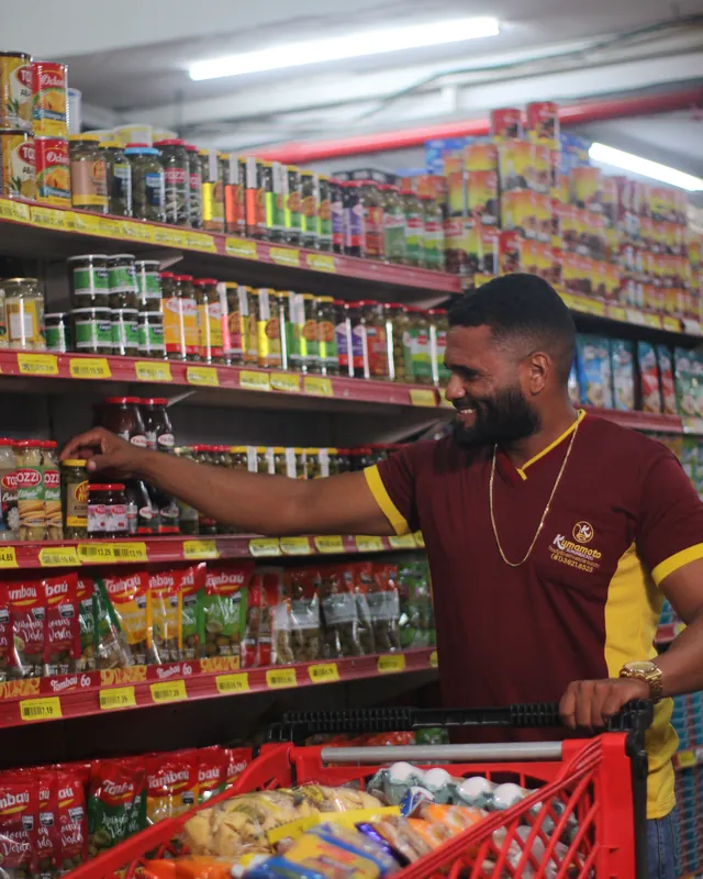 Colaborador do Kumamoto repondo produtos na gôndola, com o carrinho de reposição ao lado