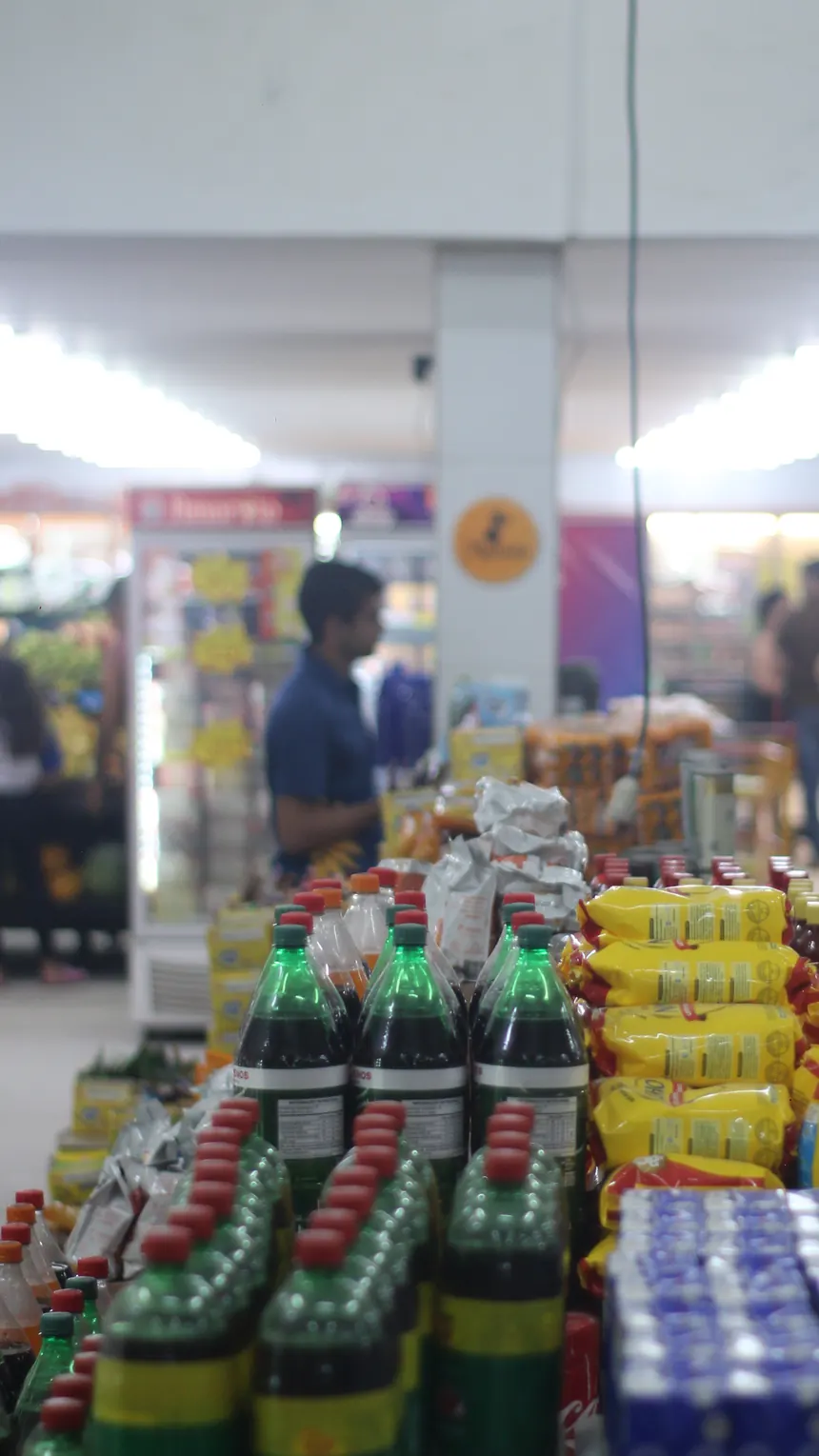 Área de frente de loja do Kumamoto com ilhas de promoção e clientes circulando com carrinho