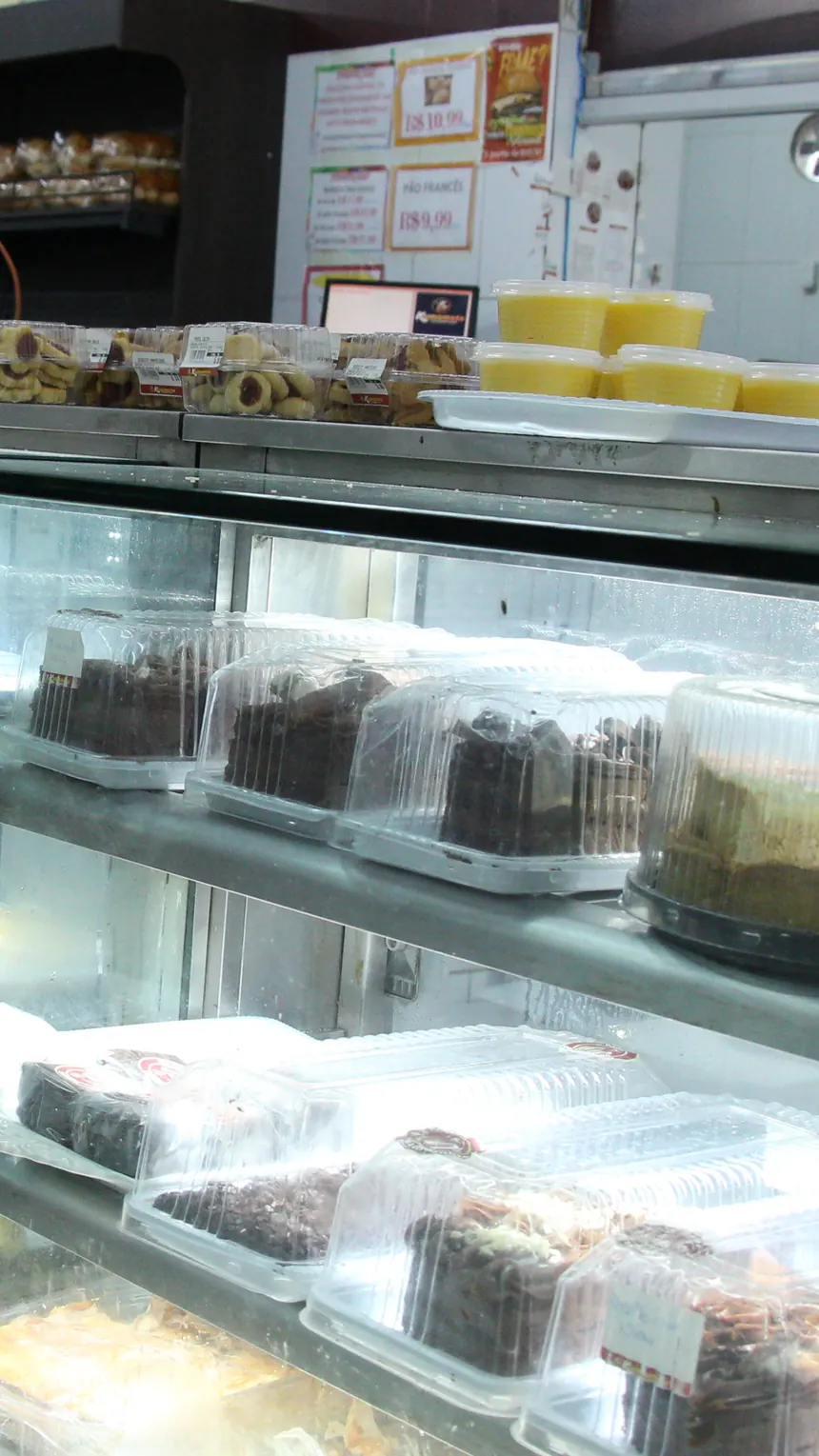 Balcão da confeitaria do Kumamoto com bolos, tortas e doces embalados sob a placa Produtos da Casa